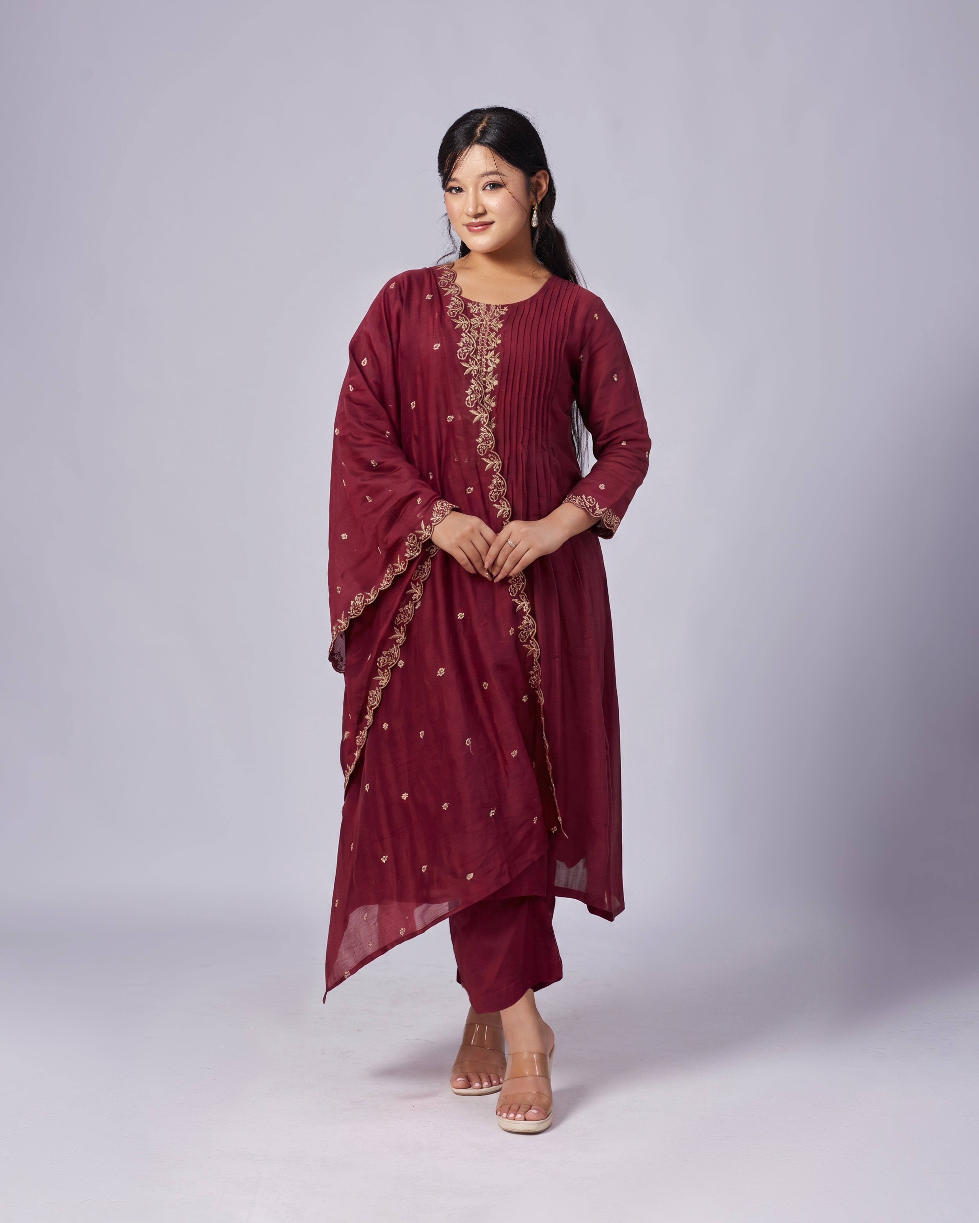 Woman wearing a maroon traditional outfit with gold embroidery on a white background