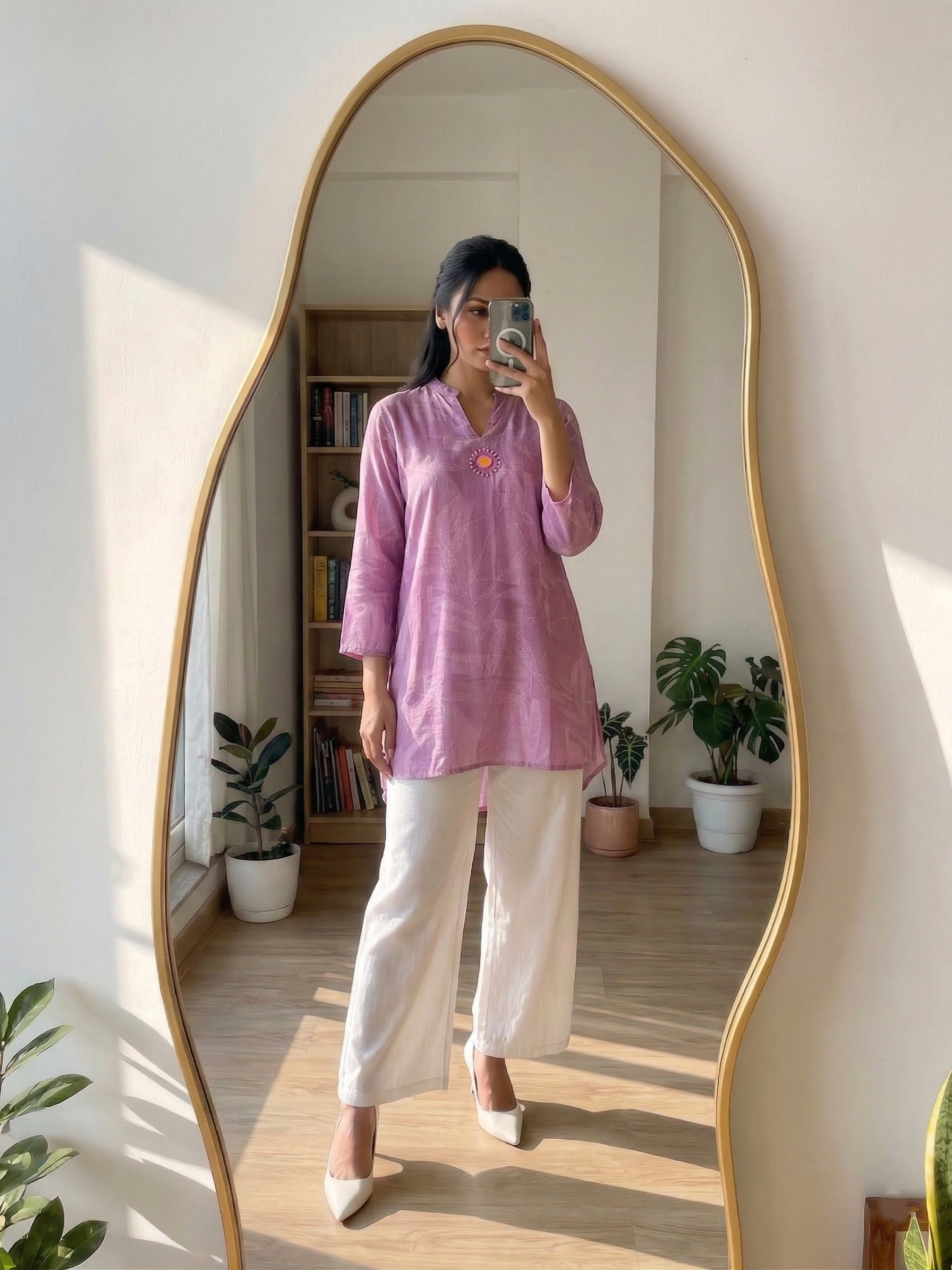 Person wearing a pink kurthi and white pants standing in front of a tall mirror.