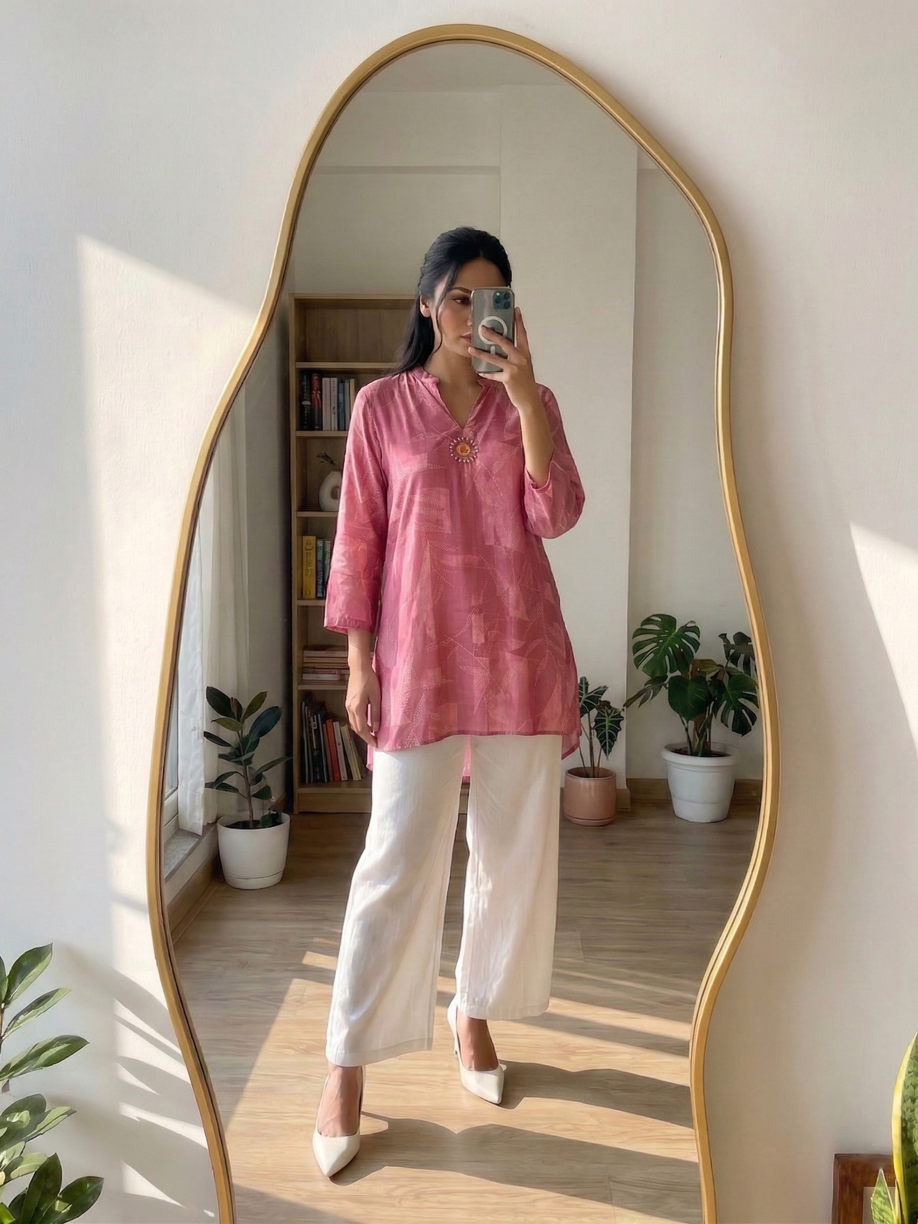 Person wearing a pink kurthi and white pants standing in front of a large mirror.