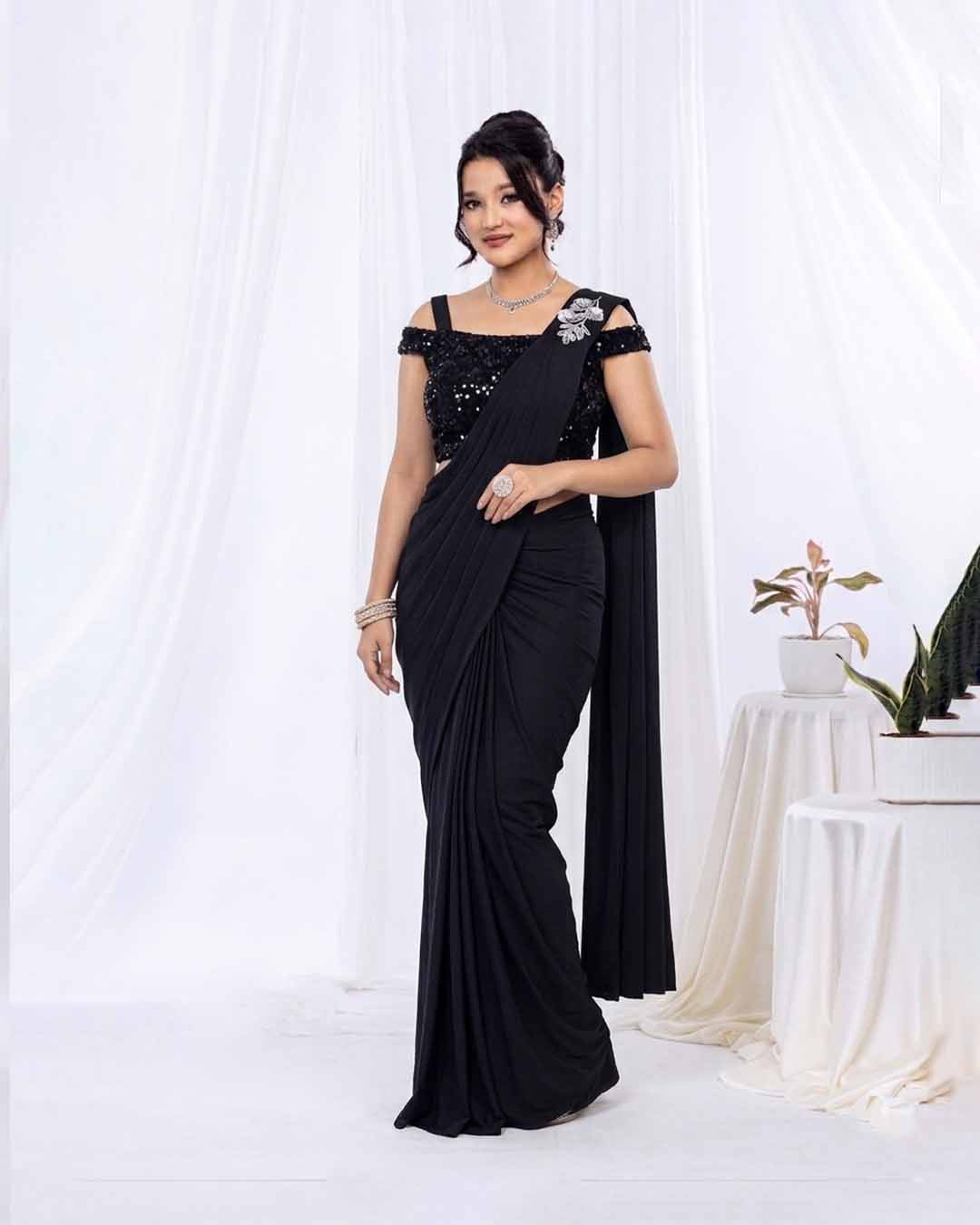 Woman wearing a black saree with silver embellishments against a white background