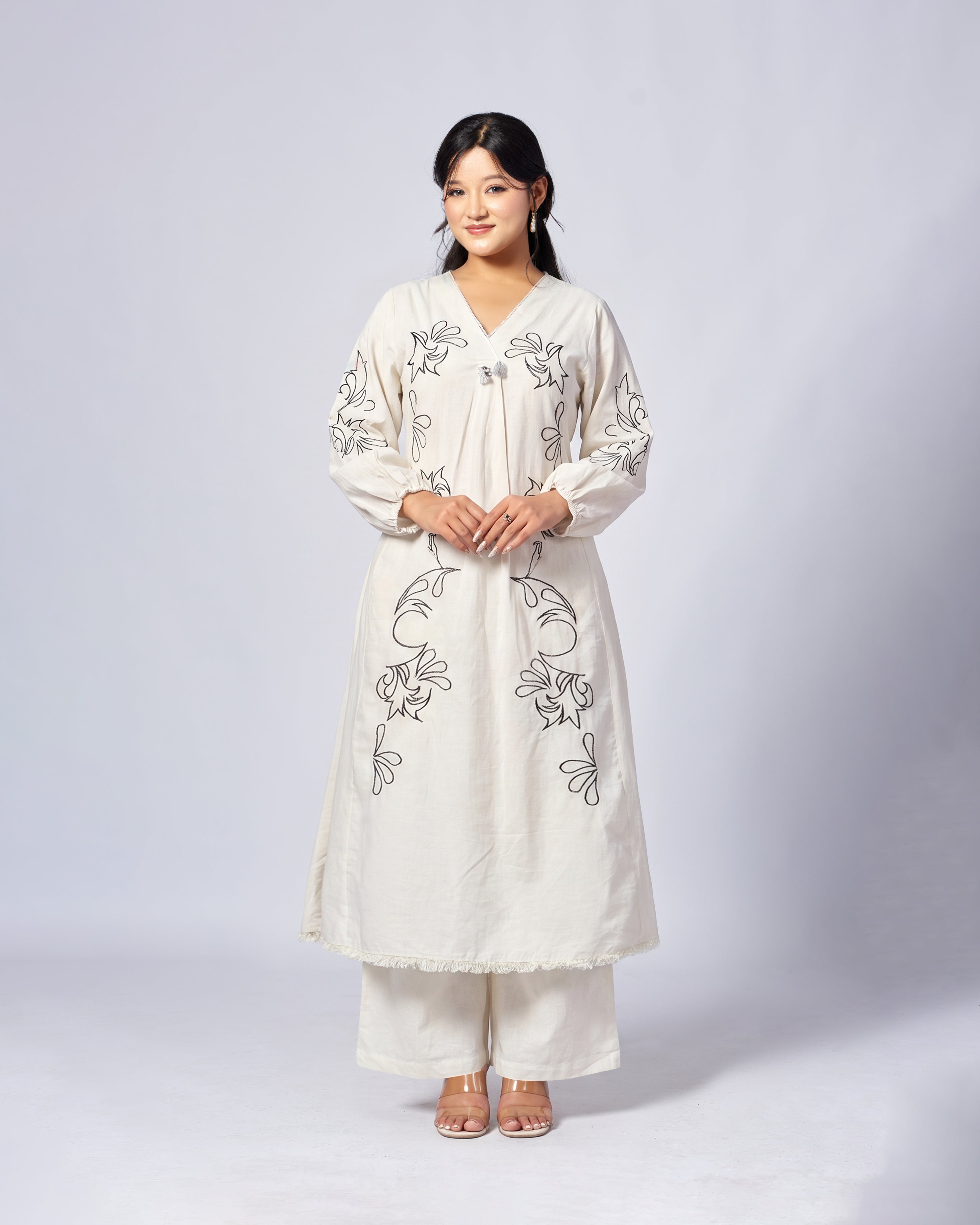 Woman wearing a white embroidered outfit on a plain background