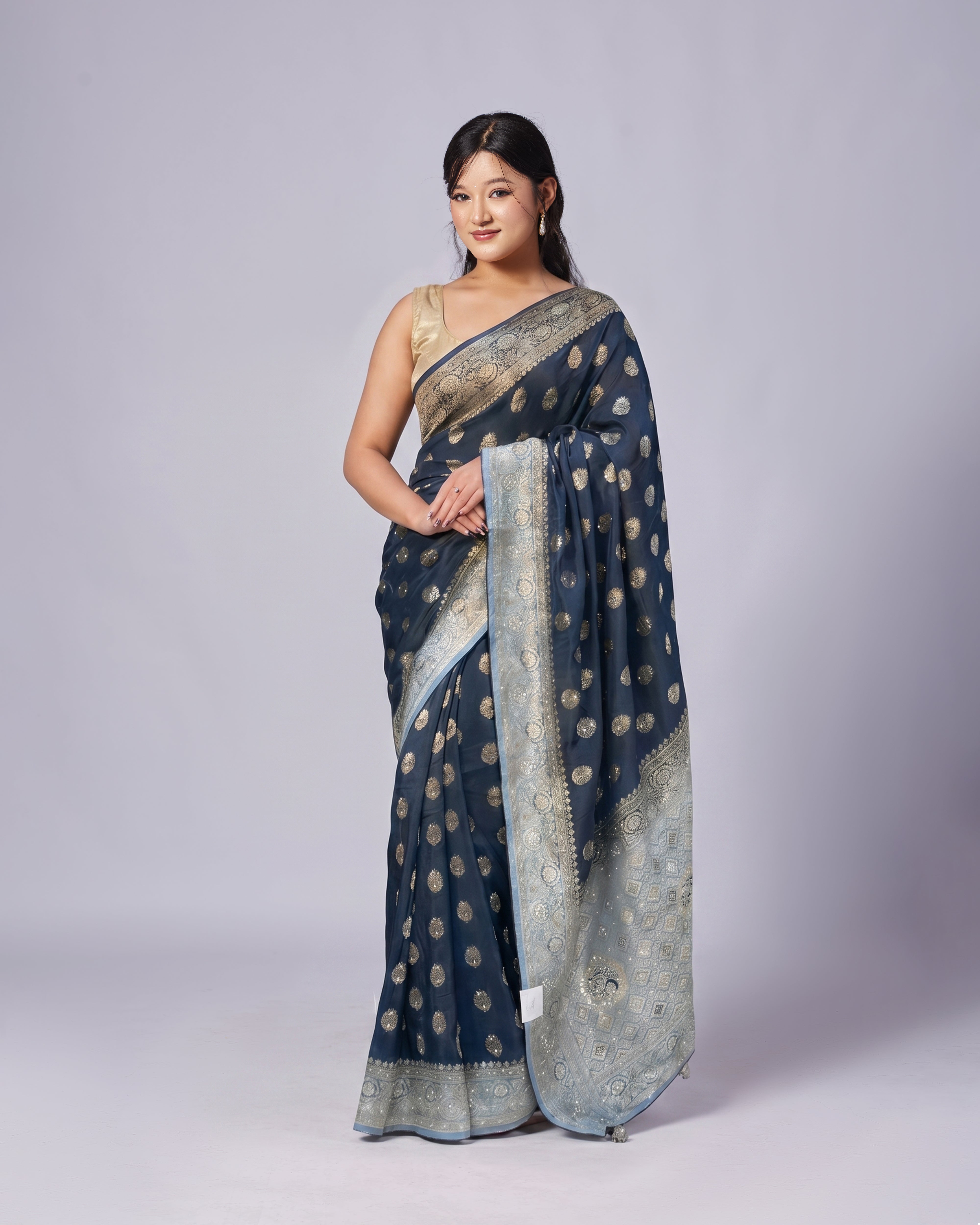 Woman wearing a blue saree with gold patterns on a gray background