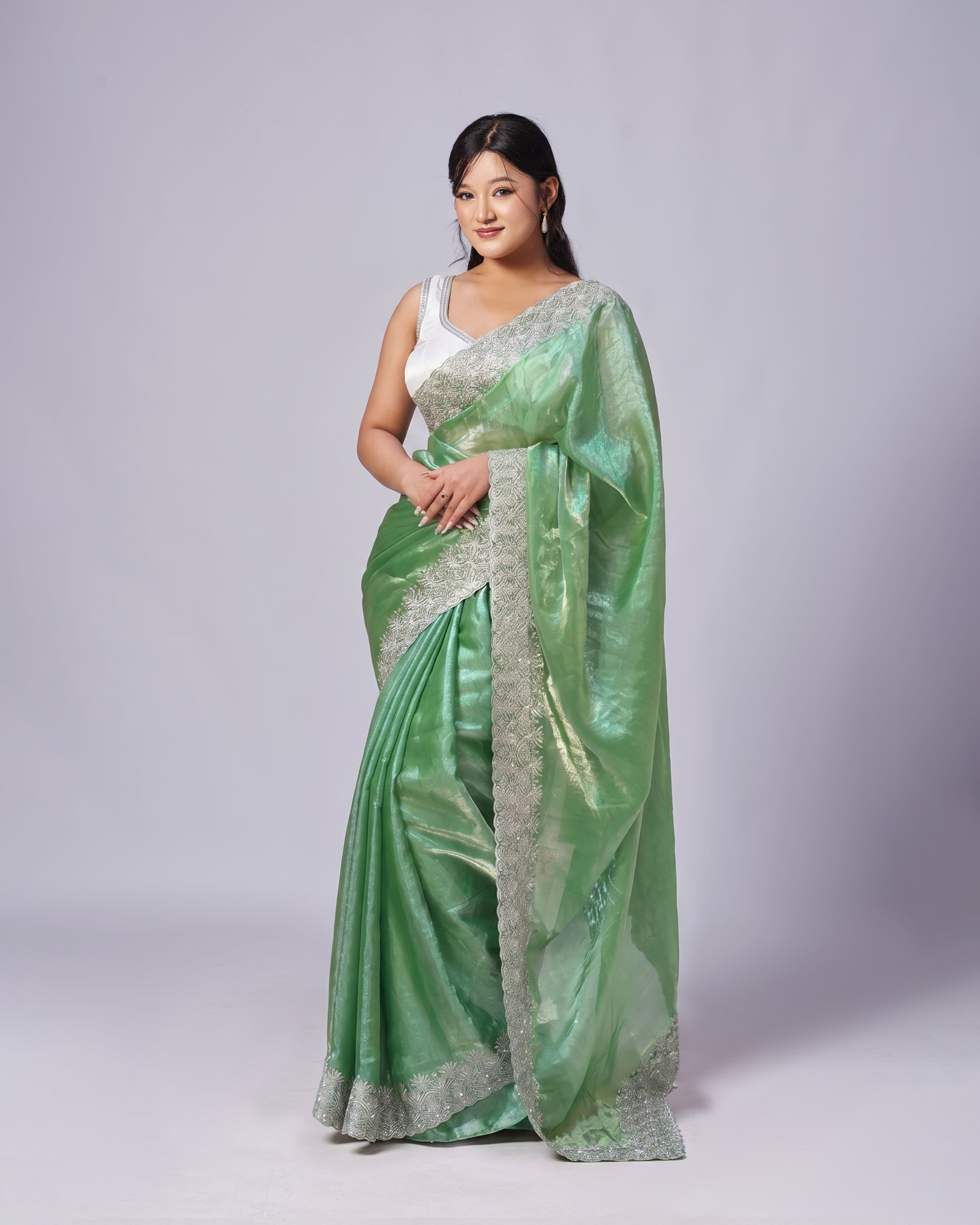 Woman wearing a green saree with a white blouse on a gray background