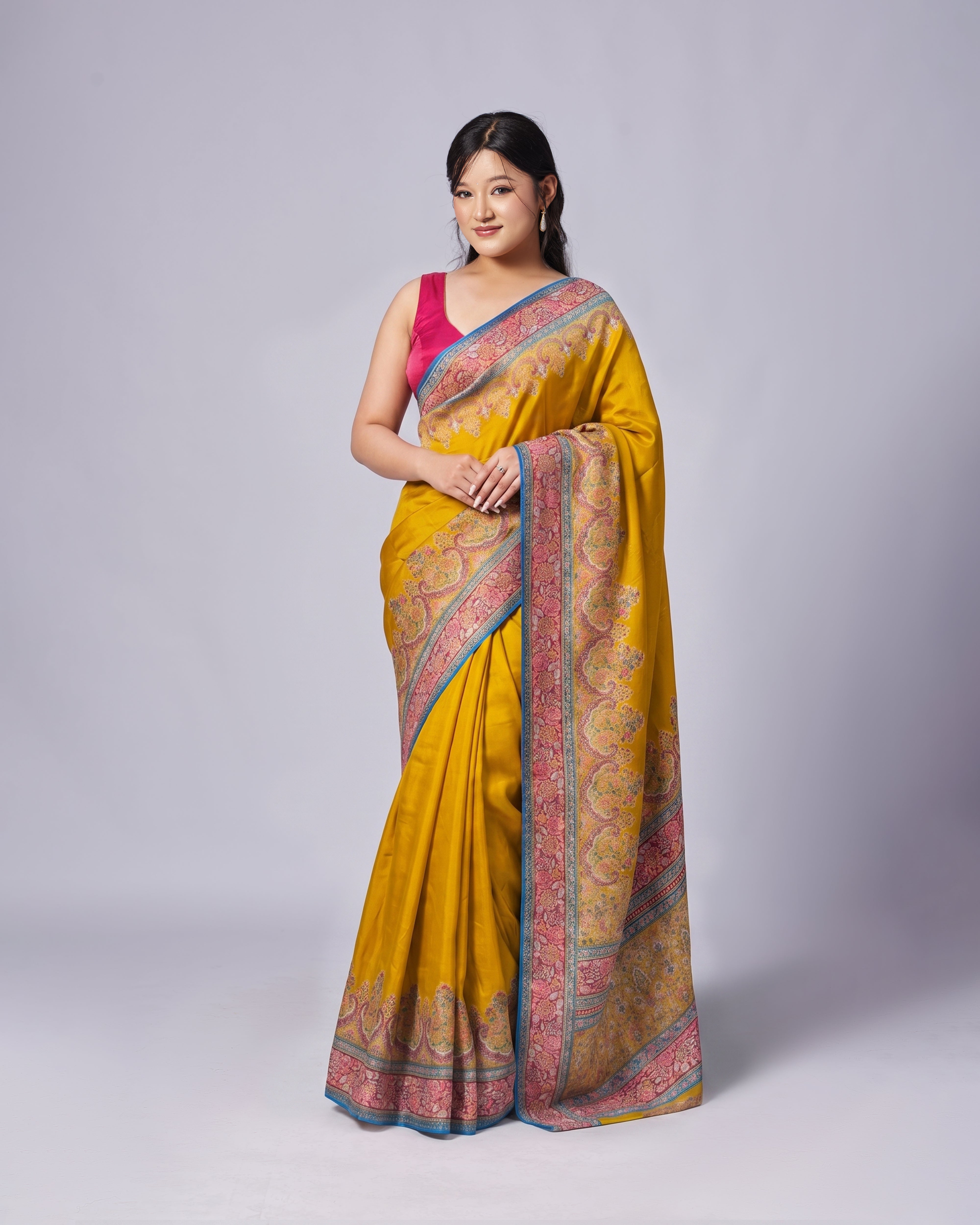 Woman wearing a yellow saree with a pink blouse on a gray background