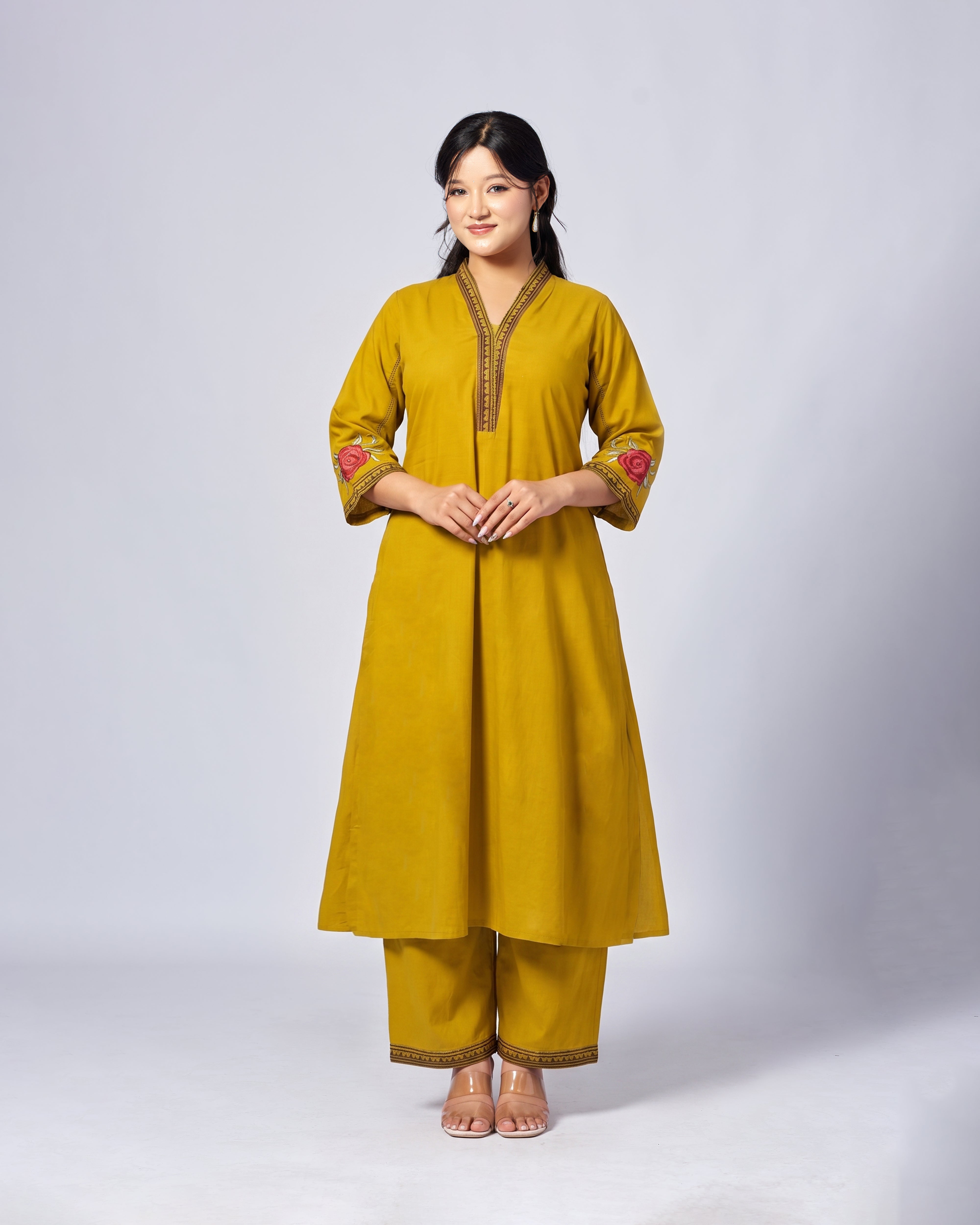 Woman wearing a mustard yellow traditional outfit with floral embroidery on a white background