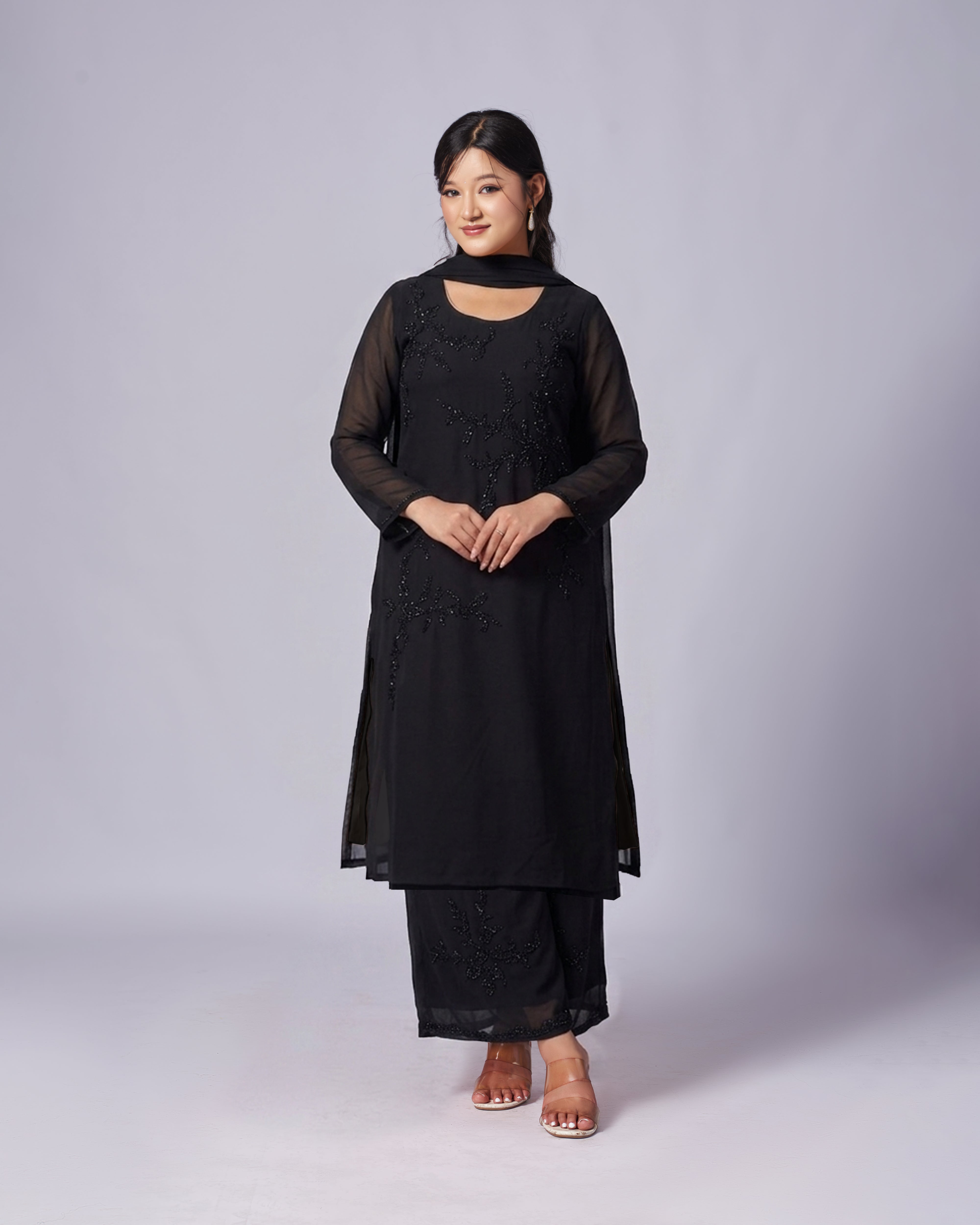 Woman wearing a black outfit with intricate designs on a plain background