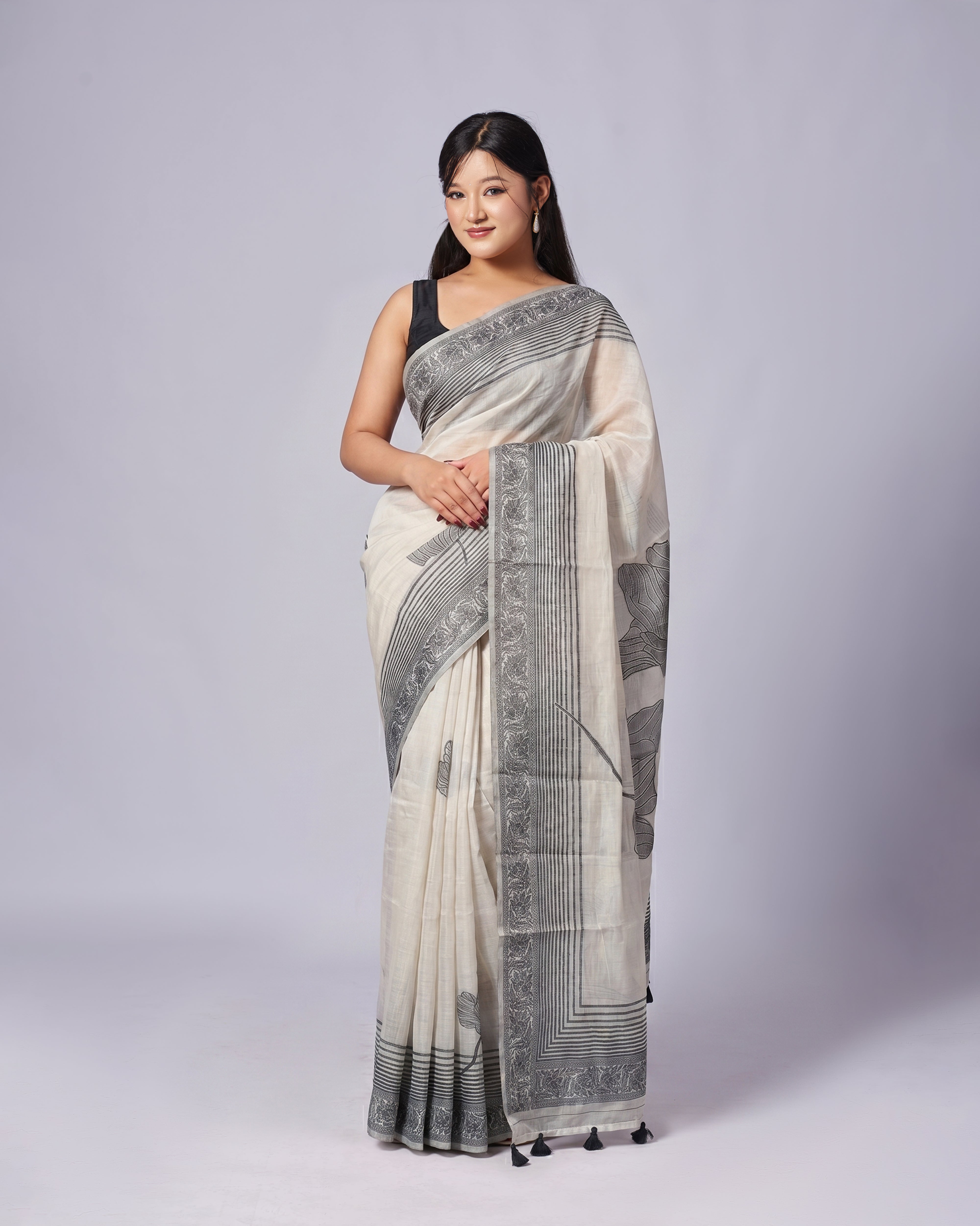 Woman wearing a white saree with black patterns on a plain background