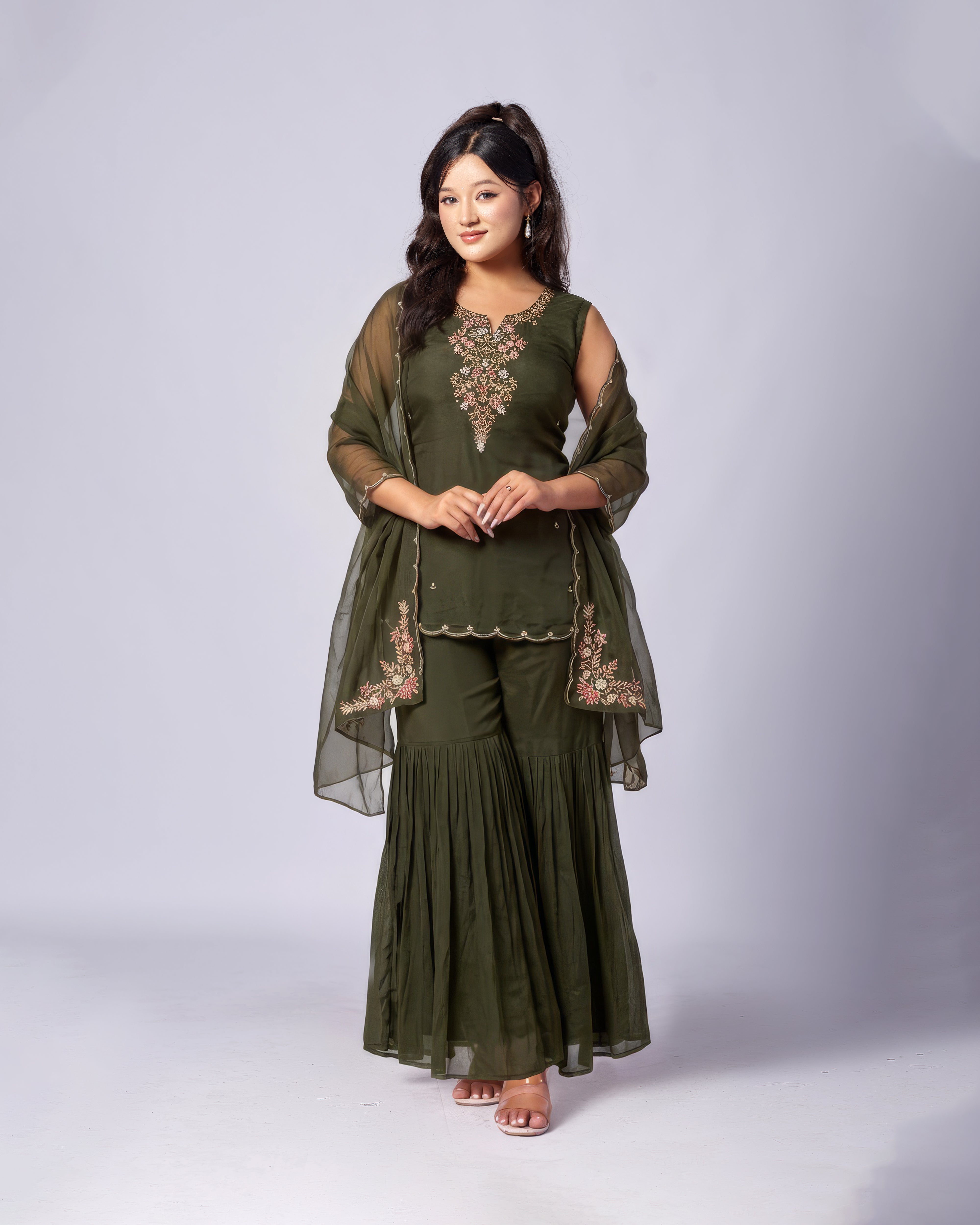 Woman wearing an olive green traditional outfit with embroidery on a white background