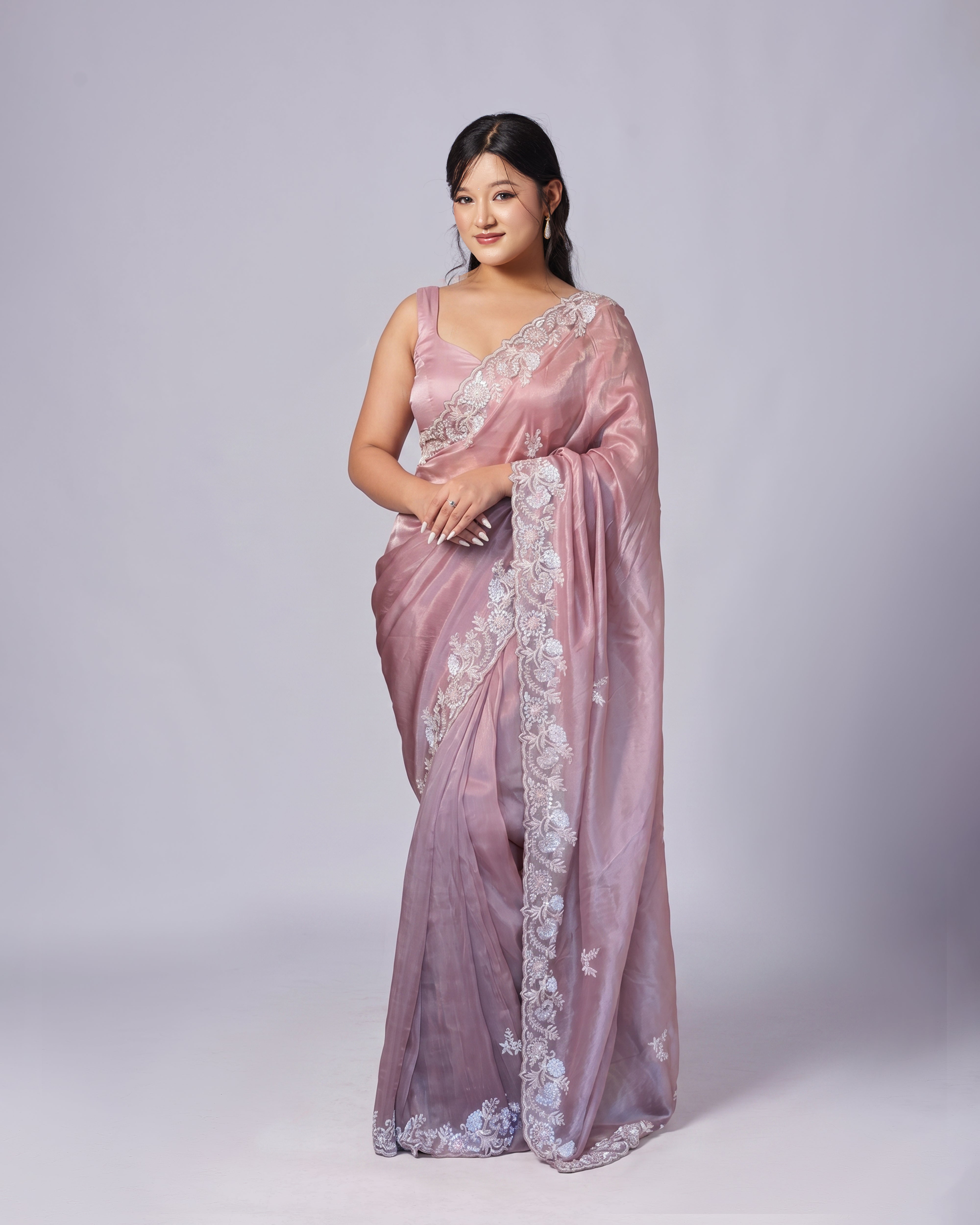 Woman wearing a pink saree with white floral embroidery on a light gray background