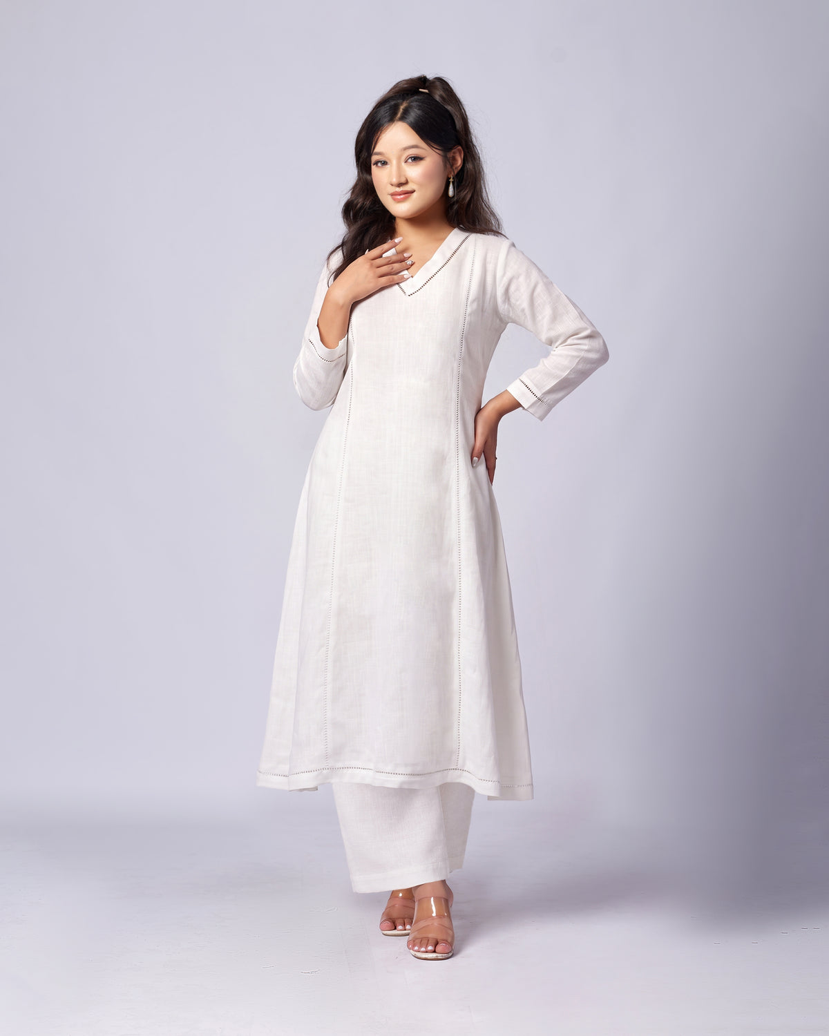 A woman modeling a white long-sleeve kurta with matching white pants, standing against a light gray studio background.
