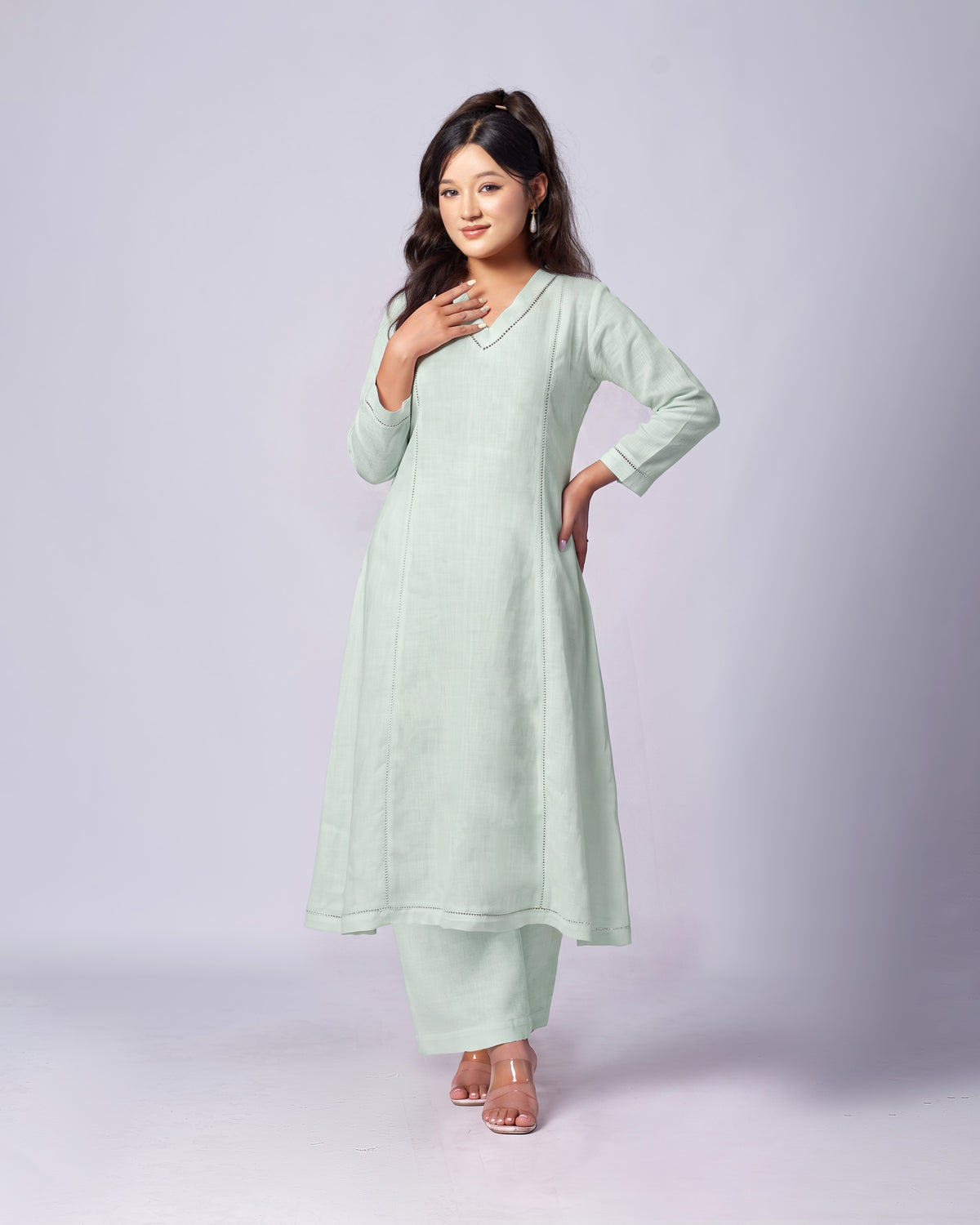 A woman modeling a light mint green long kurta and matching pants set against a plain light gray studio background.