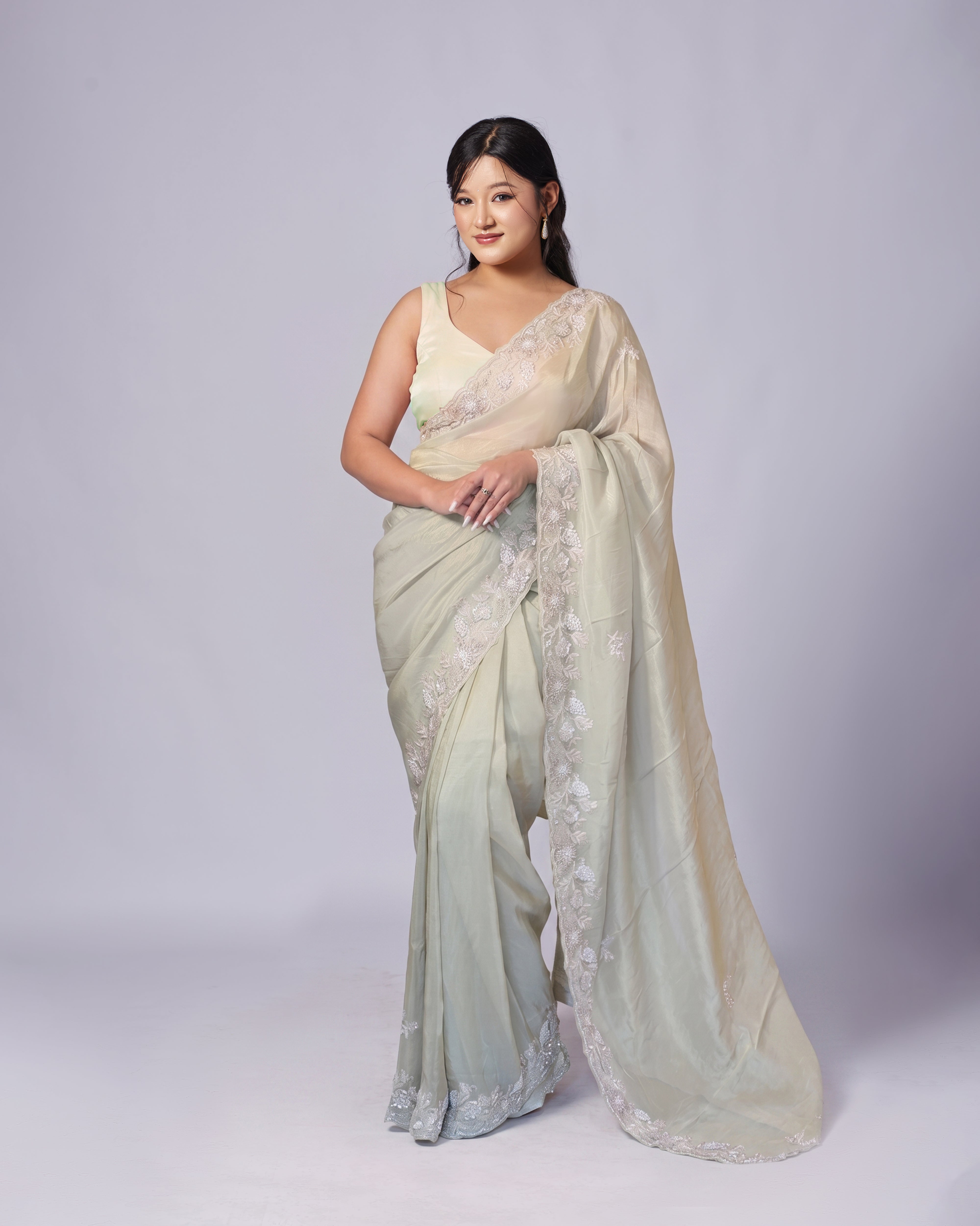 Woman wearing a light green saree with a white blouse on a gray background