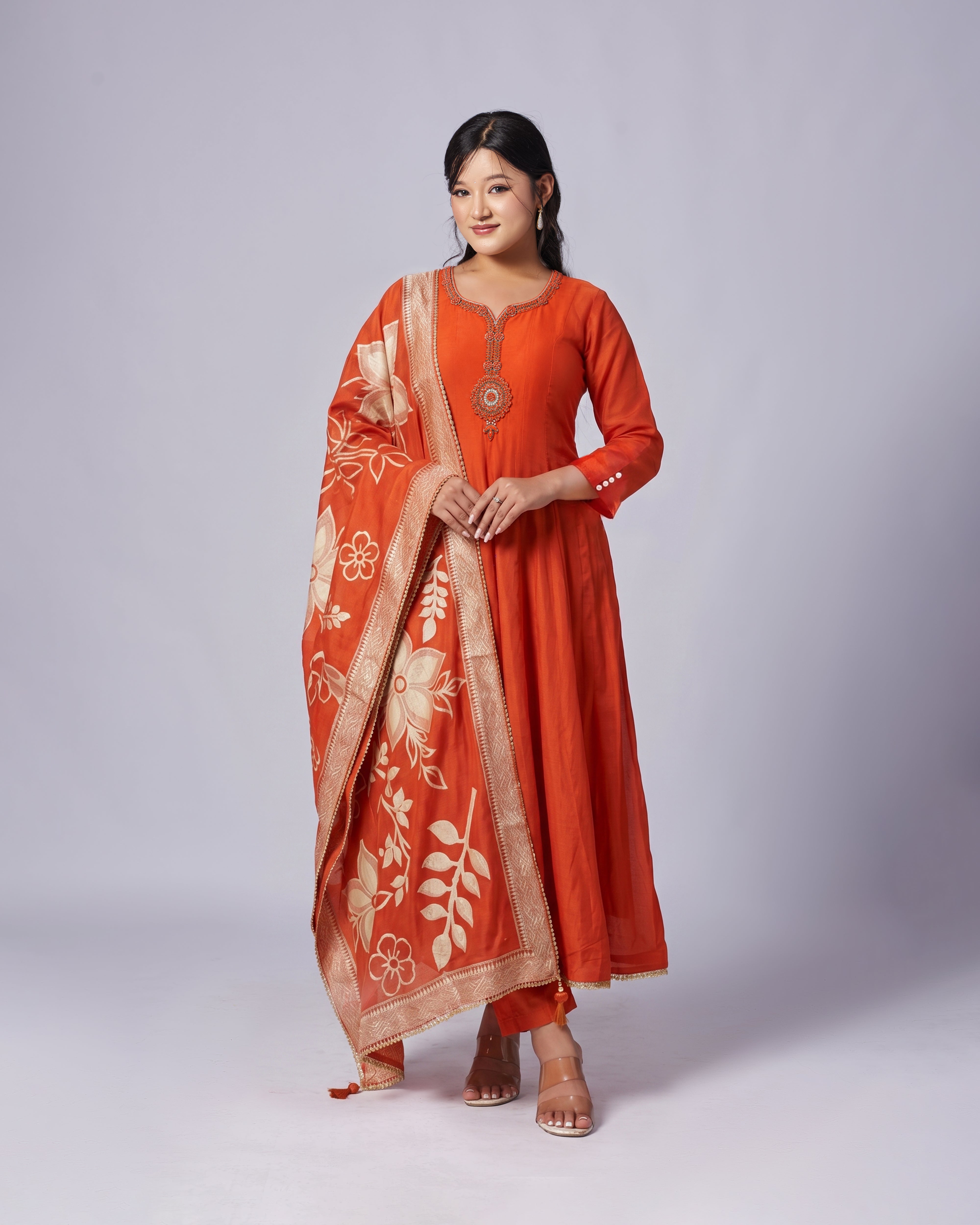 Woman wearing an orange traditional outfit with a floral pattern on a white background