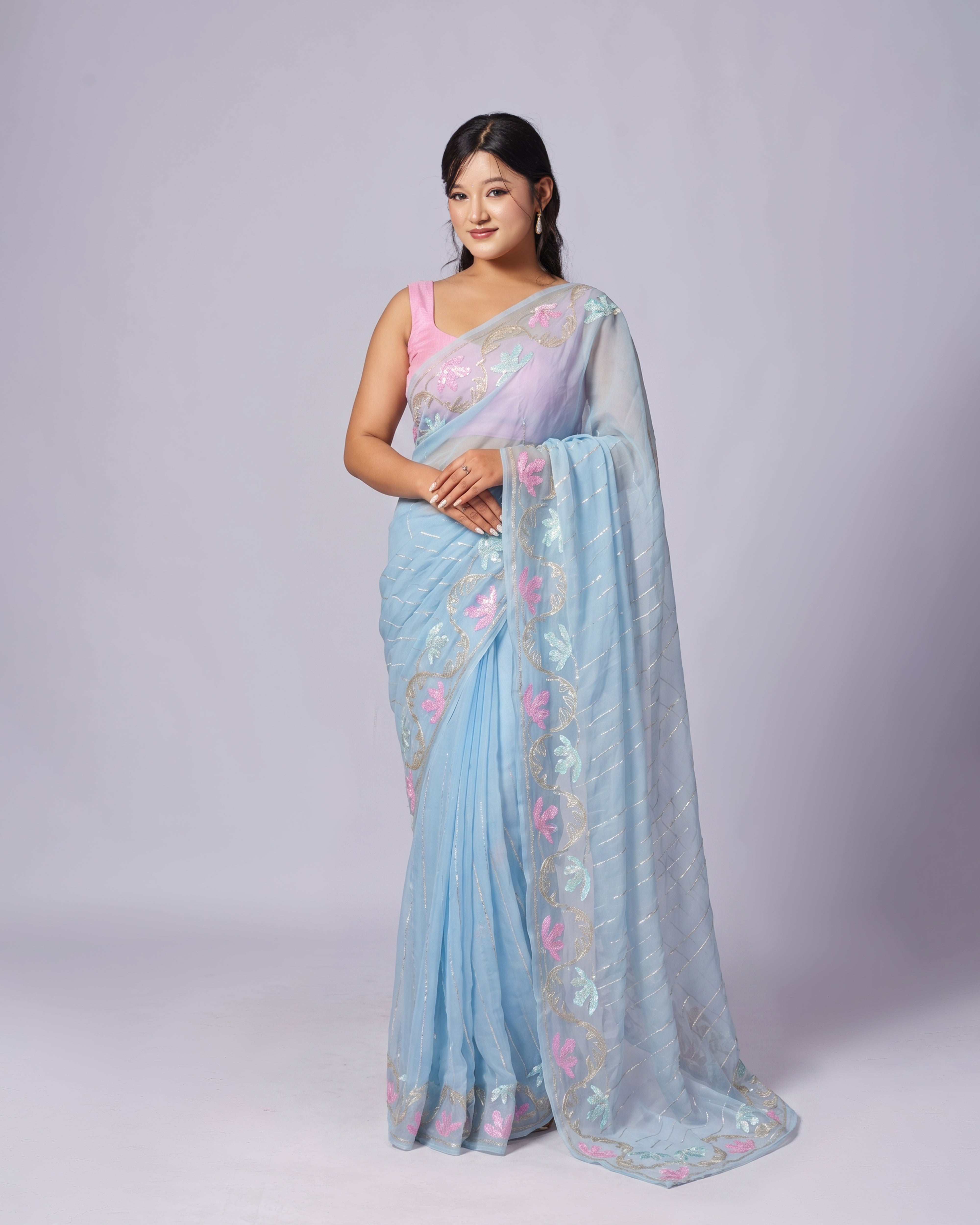 Woman wearing a light blue saree with floral patterns on a plain background