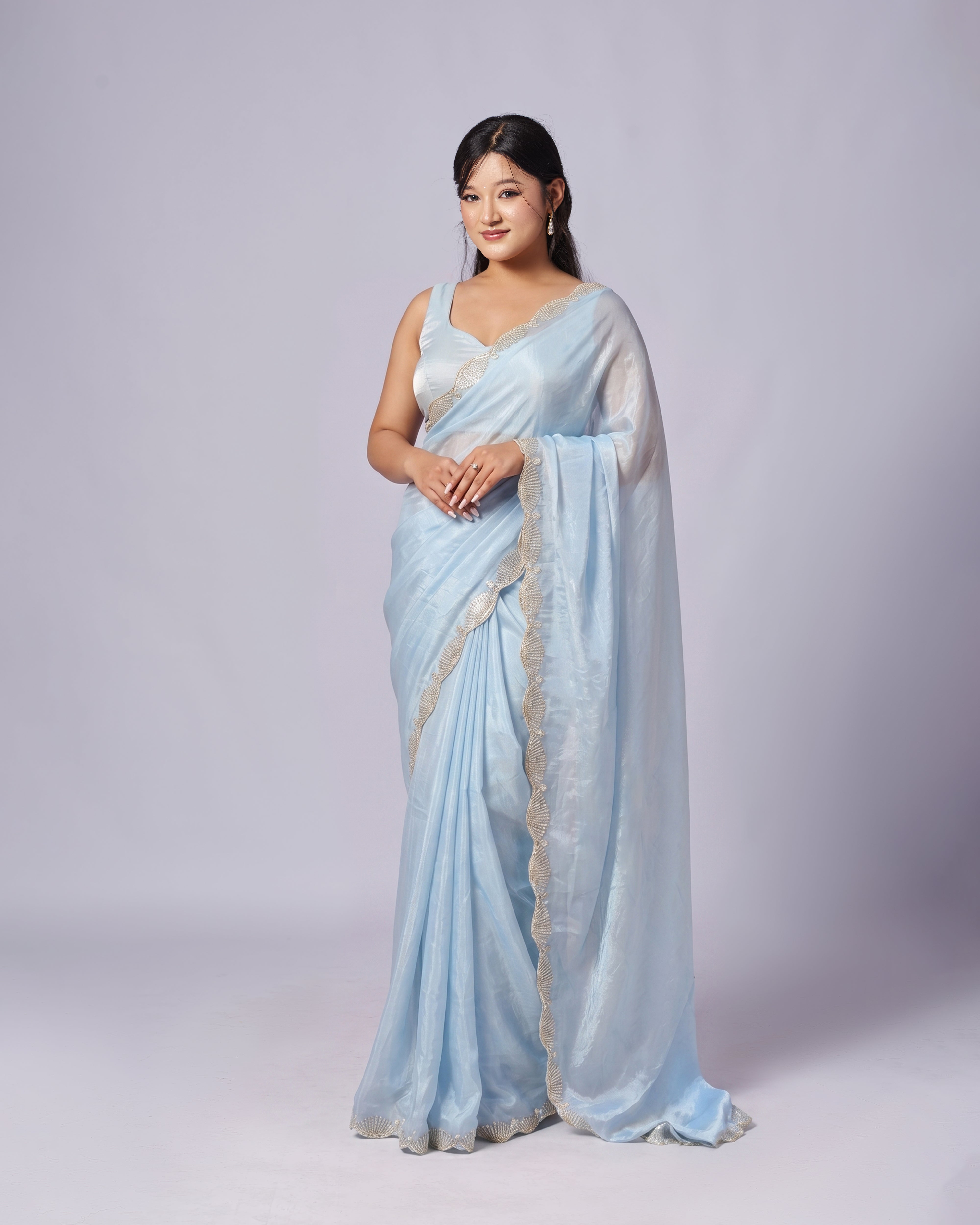 Woman wearing a light blue saree with a white blouse against a gray background