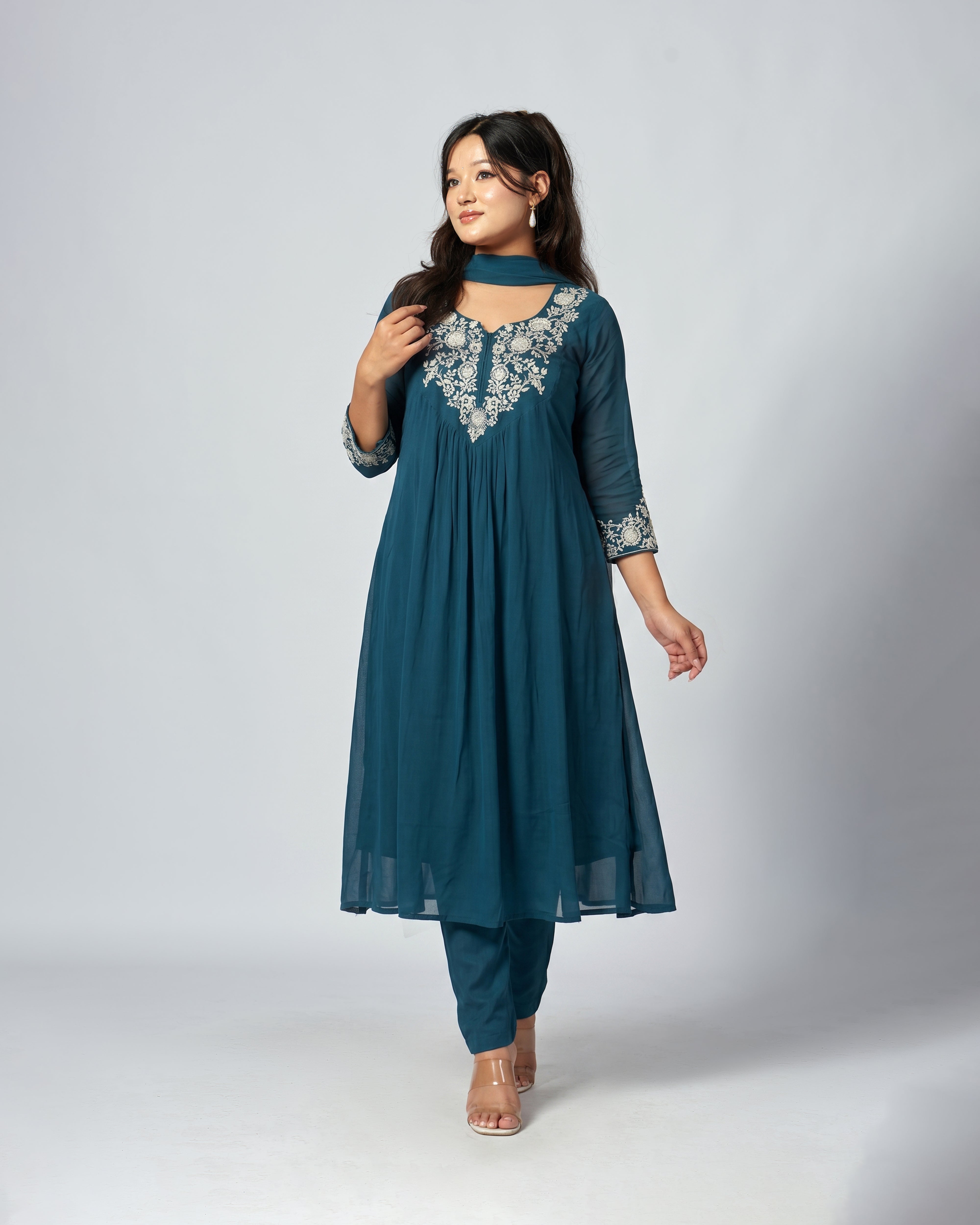 Woman wearing a teal outfit with floral embroidery on a white background