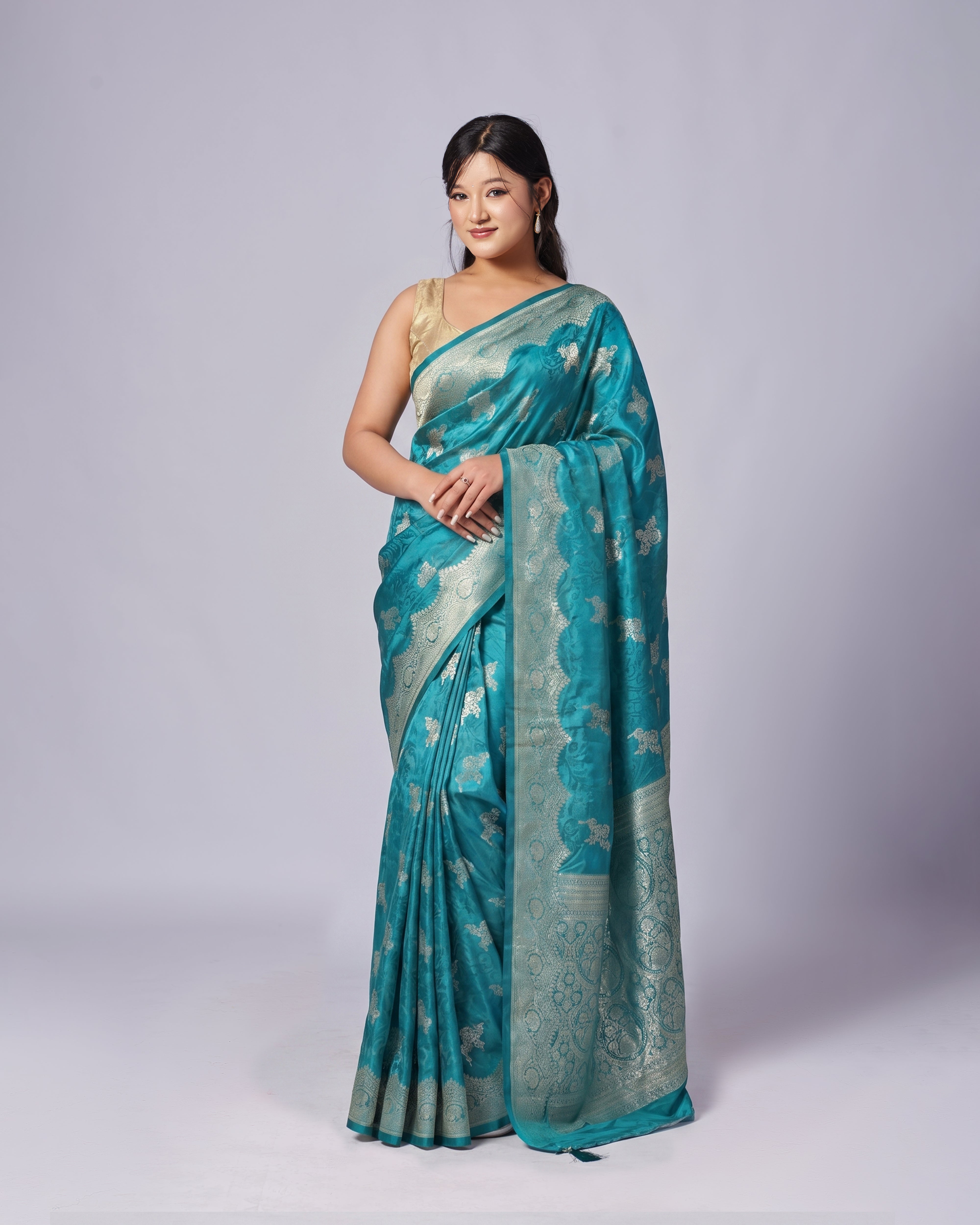 Woman wearing a teal saree with a white blouse against a gray background
